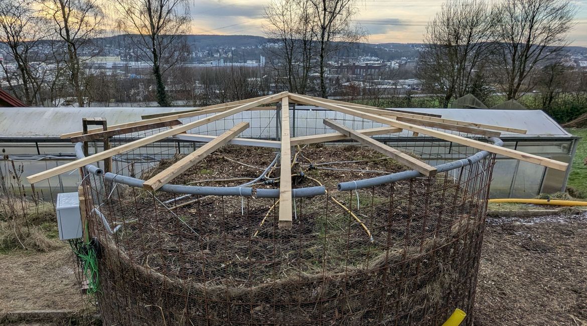 Das ist die Dachkonstruktion. Sie schützt vor Wetterereignissen, wie z.B. Schnee. Zudem schützt sie vor direkter Sonnenstrahlung, damit der Meiler nicht austrocknet.