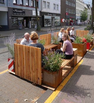Eine Gruppe menschen sitzt auf dem Parklet-Möbel in der Sonne