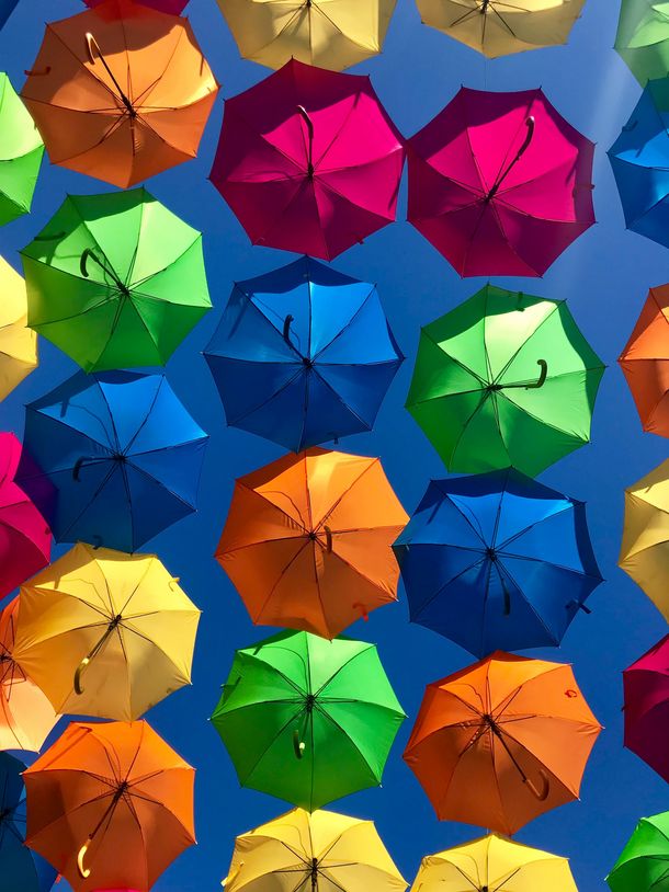 von der Sonne beschienene, aufgespannte bunte Regenschirme vor einem blauen Himmel