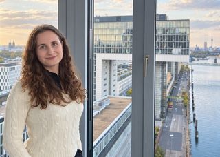 Dorothea Kretschmar hat den Masterstudiengang ‚Accounting, Auditing and Taxation‘ absolviert und arbeitet heute als Wirtschaftsprüfer bei Forvis Mazars. Ein Portrait von MAAT-Alumna Dorothea Kretschmar aus einem Gebäude mit Aussicht auf den Rhein.